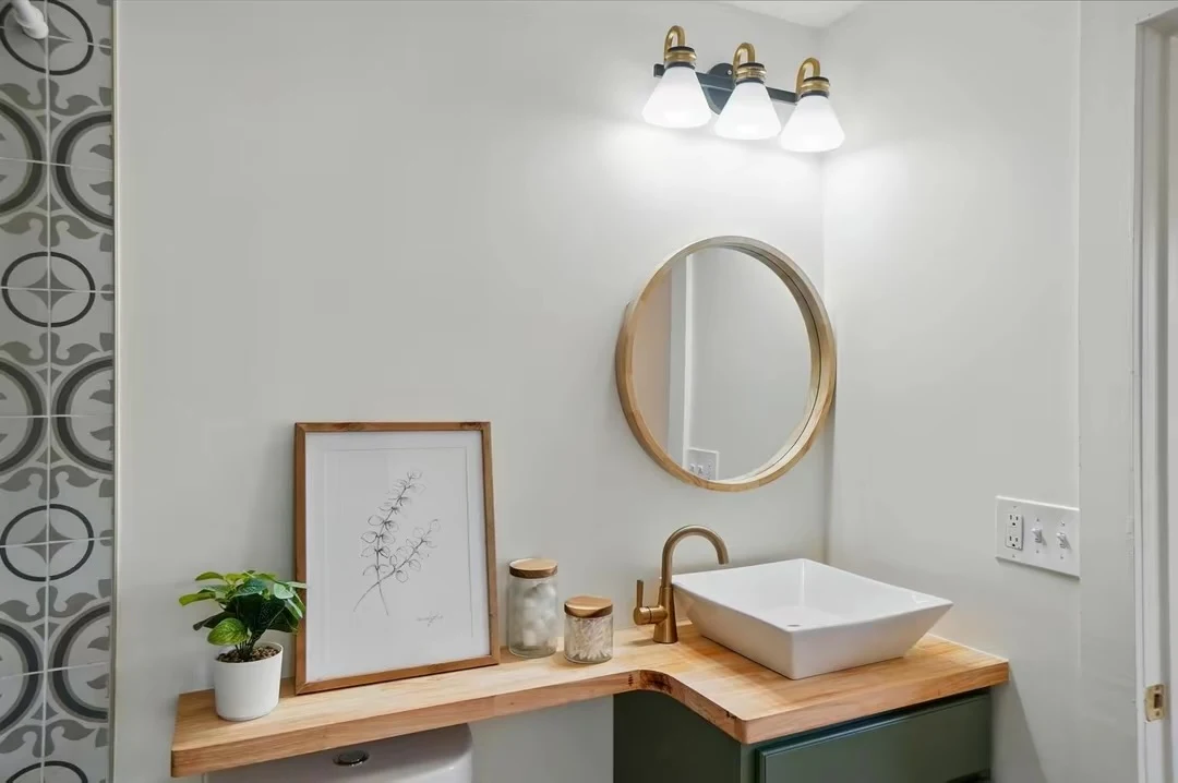 Vessel sink on a wood counter with brass faucet and round mirror
