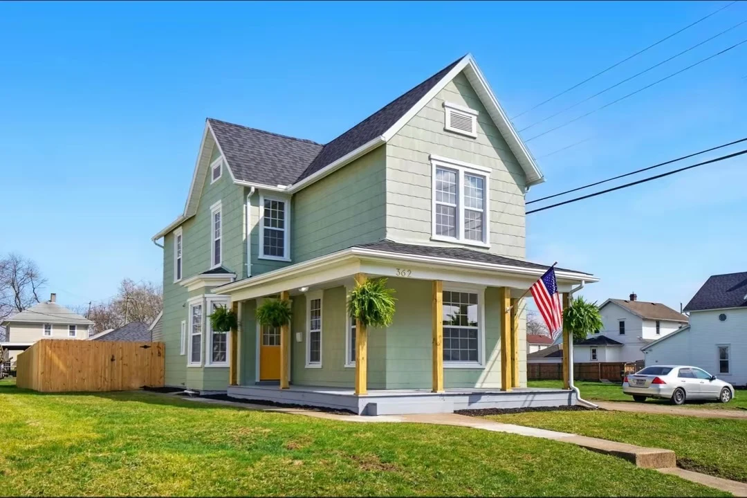 Green two-story home with covered front porch and wood posts